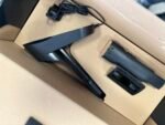 Black handheld electronic device with a plugged-in power adapter and coiled cord resting in a cardboard box.