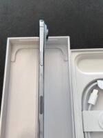 Side view of a silver smartphone standing upright in its white box, with a braided charging cable visible to the right