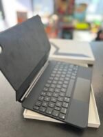 Open laptop with keyboard visible, screen angled upward, resting on a white box on a dark counter; blurred store shelves in background.