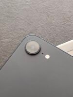 Close-up of a black smartphone corner with a circular camera lens and flash on the back surface.