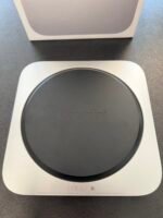 Close-up of a Mac mini in its white box, showing the round black top with the word 'Mac mini' embossed on it.
