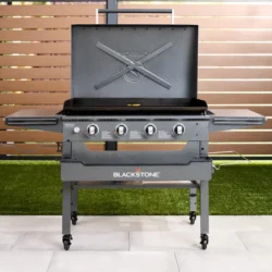 Gas-powered Blackstone grill outdoors with lid open, four control knobs, and side shelves on a wheeled stand.