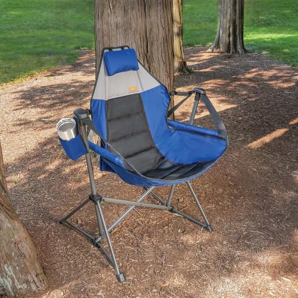 Blue and gray folding camping chair set up on dirt beside a tree, with a cup holder on the left side.