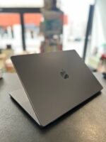 Close-up of a closed dark gray MacBook laptop on a textured counter with a blurred store interior in the background.