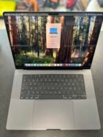Open MacBook Pro displaying a forest wallpaper with a white product card in the center showing MacBook Pro specs (16-inch, 2024).