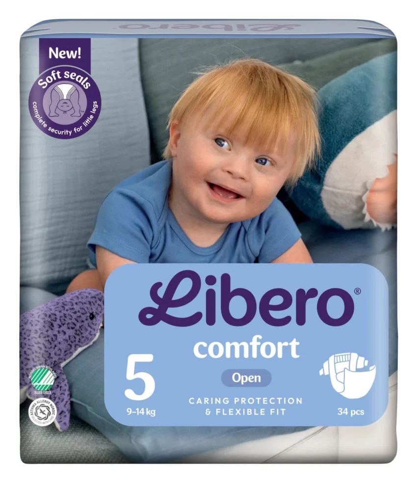 Baby smiling in a blue onesie on top of a Libero Comfort diaper package (size 5, 34 pcs) showing 'caring protection & flexible fit' label with a purple 'New! Soft seals' badge in the corner