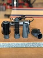 Close-up of four cylindrical hair brush attachments with bristles arranged on a wooden table, part of a styling tool set.