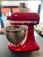 Red stand mixer with a stainless steel mixing bowl on a dark countertop, close-up view.