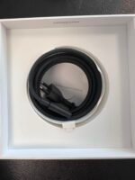 Coiled black braided cable inside a white box, with a small card reading 'Designed by Apple in California' visible in the center.