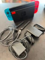 Nintendo Switch console with blue left Joy-Con and red right Joy-Con on a table, surrounded by charging adapters and cables.