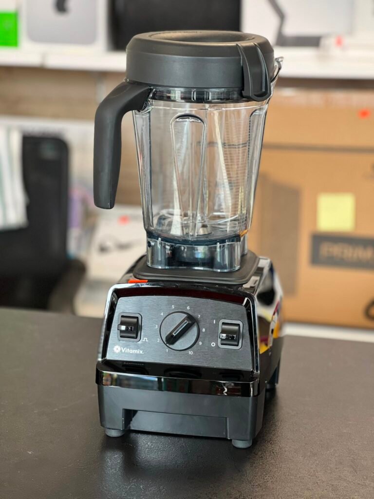 Vitamix blender with a clear pitcher and black lid on a countertop, front control dial visible.