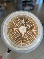 Close-up of a round metal diffuser with copper-segmented panels and many small holes in each segment.