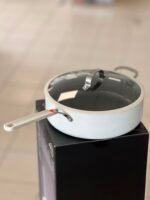 Saucepan with glass lid on a black product box in a showroom.