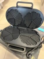 Open waffle iron showing four-leaf clover-shaped waffle grids with diamond-patterned interior surfaces in black nonstick coating.