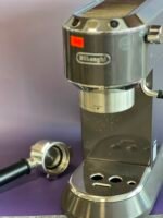 Close-up of a shiny espresso machine group head with a portafilter attached and a second portafilter nearby on a purple counter.