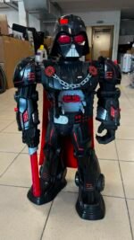 Life-size Darth Vader-style robot figure in a workshop, holding a red lightsaber and featuring red accents and a metallic chest piece.
