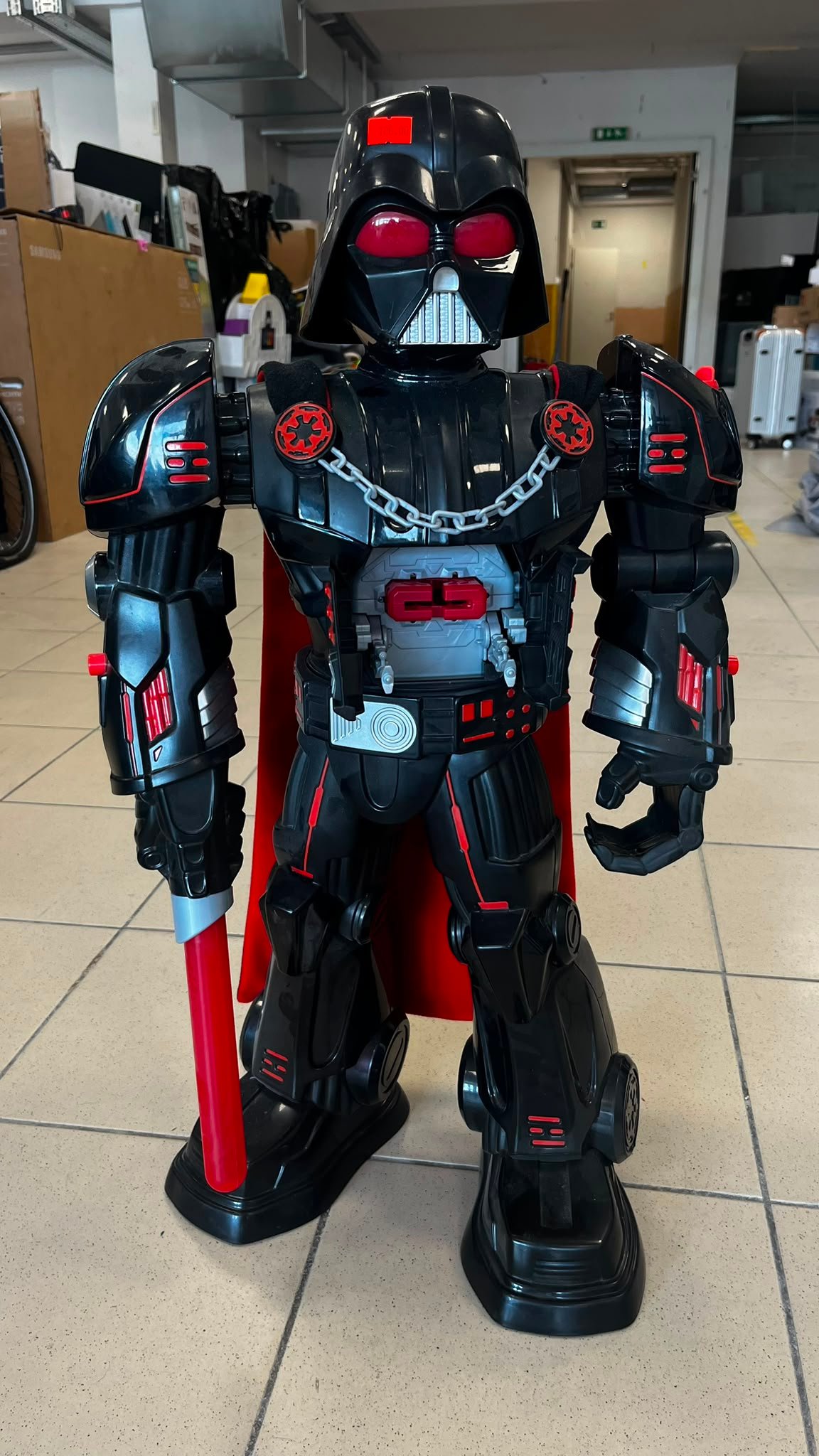 WhatsApp Image 2026-07-31 at 120217 - Radau Viska Life-size Darth Vader-style robot figure in a workshop, holding a red lightsaber and featuring red accents and a metallic chest piece.