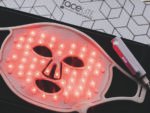Red LED facial treatment mask lit up in pink, with a white frame on a dark surface beside a 'Face Lite' box.