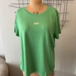 Green DKNY T-shirt displayed on a fashion mannequin with an abstract black metal wall sculpture behind it.