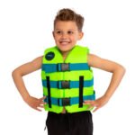 Smiling boy in a neon green life jacket with blue straps, standing with hands on hips against a white background.