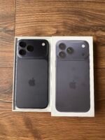 Two opened iPhone boxes showing the back of dark-gray phones with triple-camera modules on a wooden surface