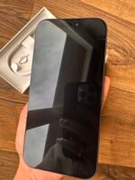 Black smartphone held above its white box with charging accessories on a wooden table.