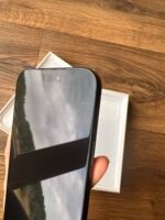 New smartphone being unboxed, held over an open white box on a wooden floor, with the screen facing up.