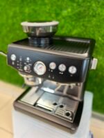 Close-up of a black espresso machine with a portafilter attached to the group head and chrome gauges in the foreground.