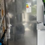 LG stainless steel refrigerator/freezer standing upright in a utility room, with energy rating label and warranty stickers visible on the door