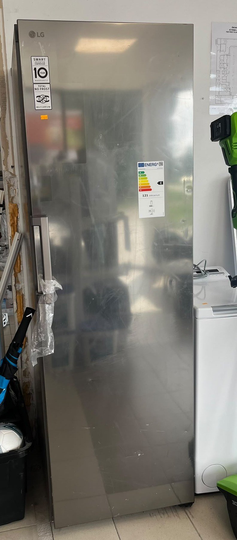 WhatsApp Image 2026-08-01 at 110758 - Radau Viska LG stainless steel refrigerator/freezer standing upright in a utility room, with energy rating label and warranty stickers visible on the door