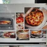 Box showing a 'Pizza Oven' by Cuisinart with collage of pizzas and an oven image on the front panel, product packaging visible in a showroom.