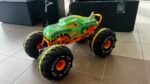 Colorful green toy monster truck with oversized black tires and bright orange suspension on a tiled floor indoors, resembling a display model.