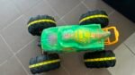 Top-down view of a bright green toy monster truck with large black tires and yellow wheel rims on a tiled floor.