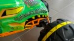 Close-up of a neon green Hot Wheels toy car with orange suspension and a large black-tread tire with a yellow stripe.