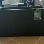 Large black outdoor storage box with a green Deroma Millennium tag attached to the side of the box in a showroom setting