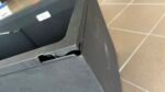 Cracked corner of a dark metal frame with visible interior gap and torn edge near a tiled floor area.