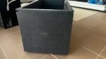 Open-top black metal storage box with empty interior on a tiled showroom floor