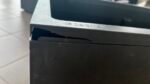 Close-up of a damaged corner of a black electronic device with a silver edge and embossed brand name.
