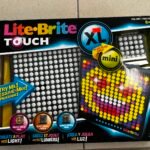 Lite-Brite Touch XL toy packaging with a grid of colorful pegs on display, on a tiled floor.