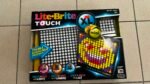 Lite-Brite Touch XL toy packaging with a grid of colorful pegs on display, on a tiled floor.