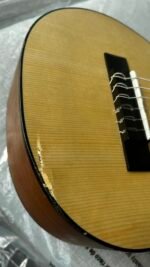 Close-up of a wooden guitar body showing strings and bridge on the right, with a chipped edge along the rim indicating damage or wear.