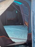 Inside a blue sleeping area: empty tent with a blue sleeping bag and dark interior, gear stored along the sides.