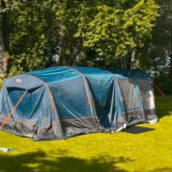 Blue and gray Camping tent pitched on a sunny grassy lawn with tall trees behind it.