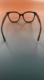 Black square eyeglasses with tortoiseshell temples resting on a gradient peach-to-gray background.