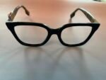 Close-up of black plastic eyeglasses with clear temples resting on a pale surface, viewed from below.