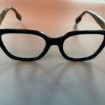 Close-up of black plastic eyeglasses with clear temples resting on a pale surface, viewed from below.