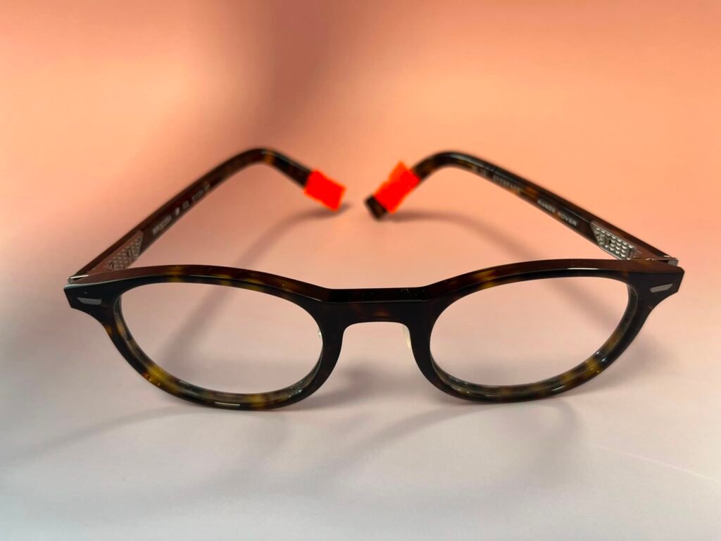 Close-up of black tortoiseshell eyeglasses with orange nose pads on a light background.