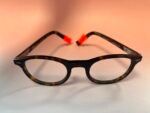 Close-up of black tortoiseshell eyeglasses with orange nose pads on a light background.