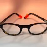 Close-up of black tortoiseshell eyeglasses with orange nose pads on a light background.