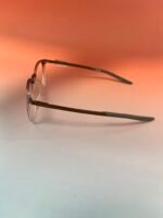 Pair of metal-framed eyeglasses resting on a pale surface with an orange gradient background behind them.
